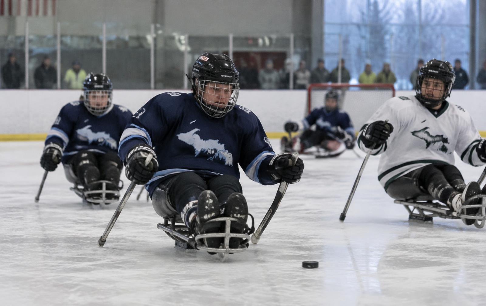 Adaptive athletes playing sled hockey in a community ice rink