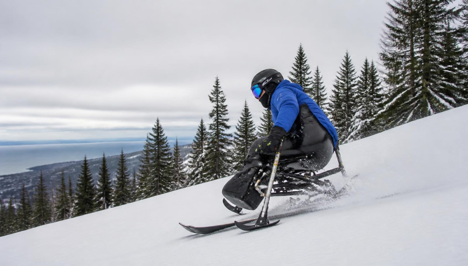 An adaptive sit-skier with outriggers carving down a groomed ski run above Lake Superior